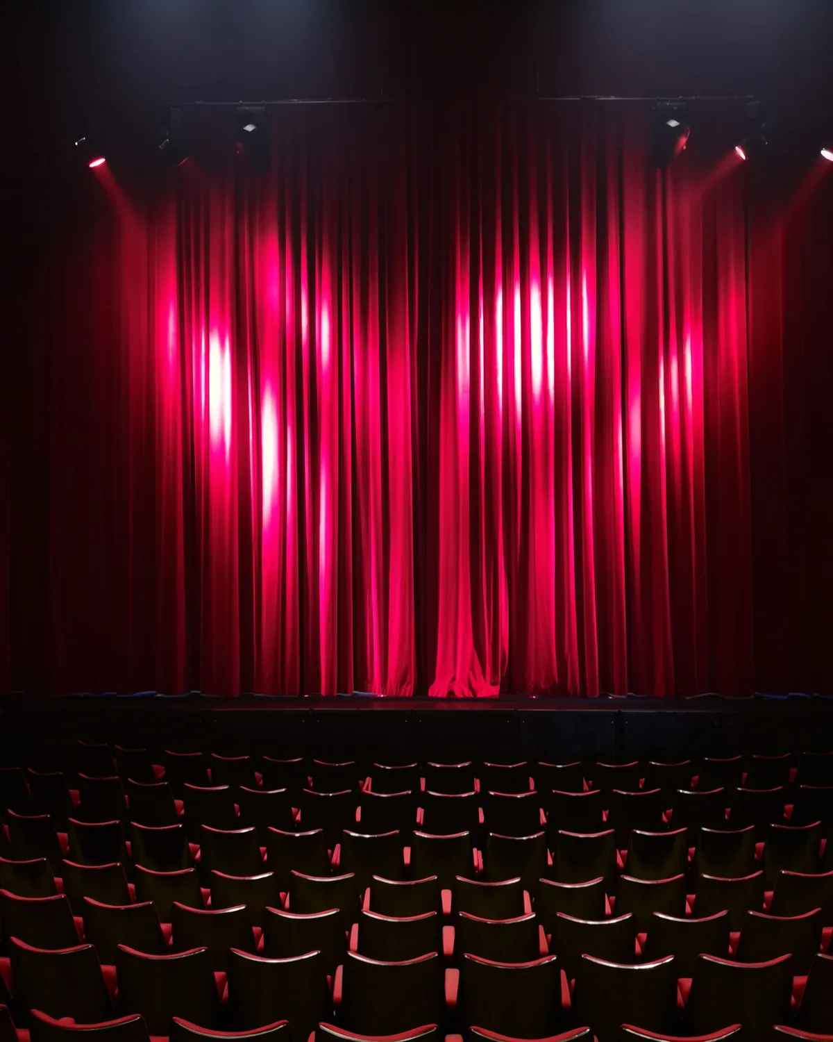 Ein roter Bühnenvorhang, beleuchtet über Reihen leerer Theatersitze