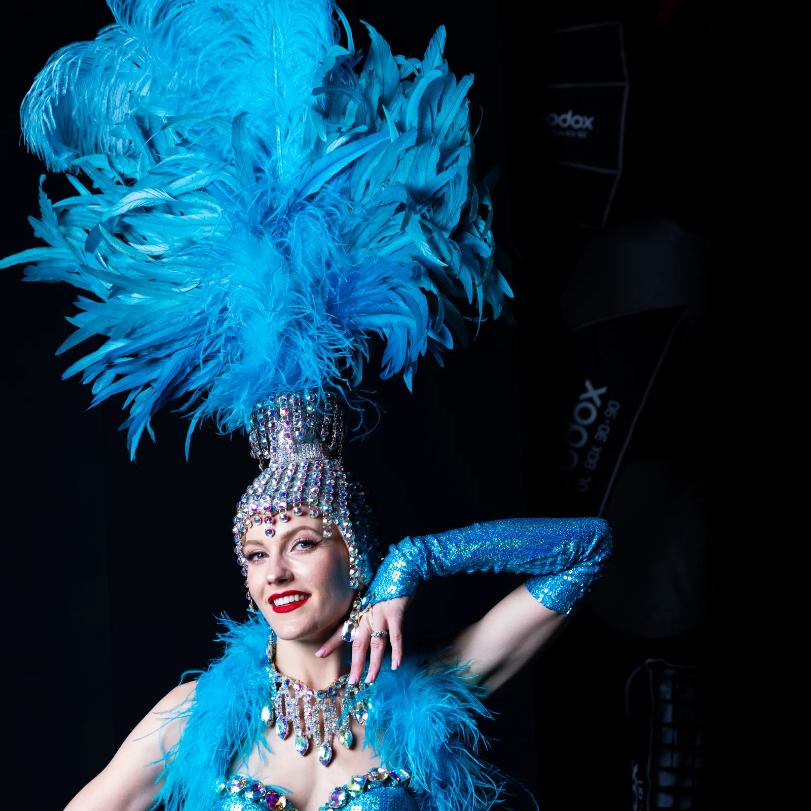 Eine Showgirl mit Federkopfschmuck und Paillettenkostüm, beleuchtet vor dunkler Bühne